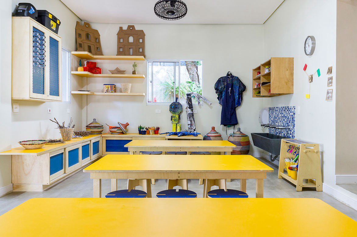 sala didática cozinha infantil com moveis de marcenaria, bancada, mesas de tampo amarelo e bancos com laminado azul, armarios e prateleiras