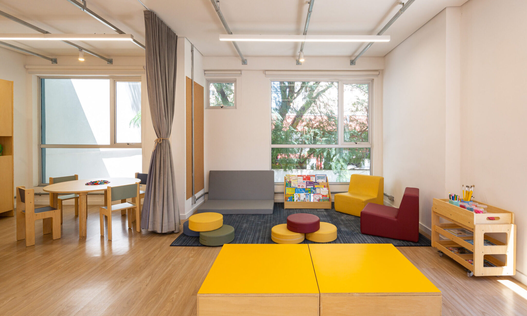 escola Camino, ambiente aberto com estofados infantis, cadeiras e mesa, biblioteca com livros