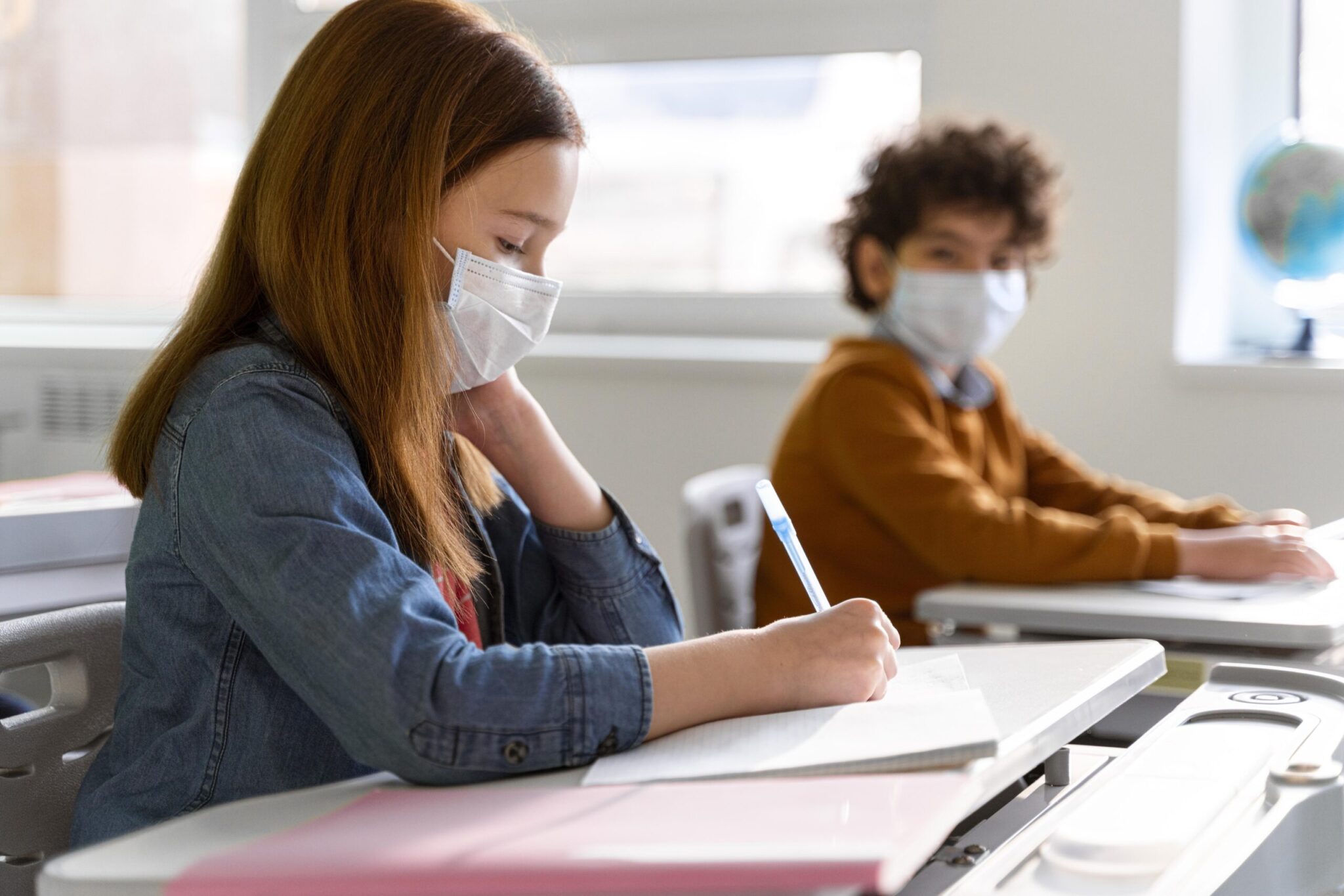 duas crianças com mascaras cirurgias estudando em sala de aula
