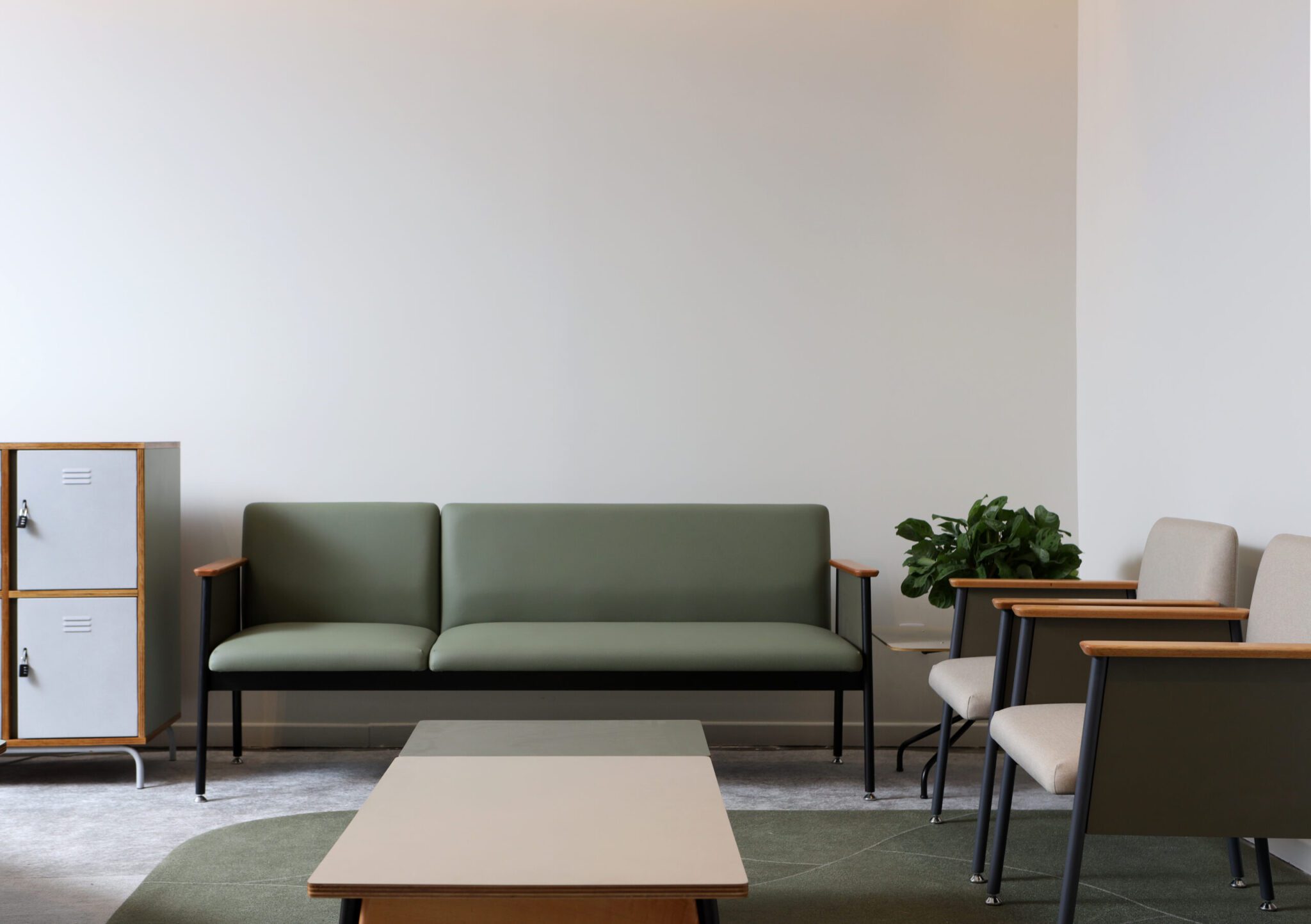 Estande da SP-Arte com um sofá, duas poltronas, uma planta lateral e uma mesa de centro sobre um tapete verde